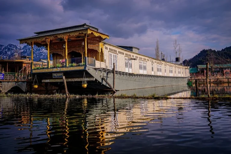 Luxury traditional houseboat on Dal Lake in Srinagar with mountain views and reflections on the water, featured in the Kashmir Honeymoon Package: 5 Nights /6 Days.